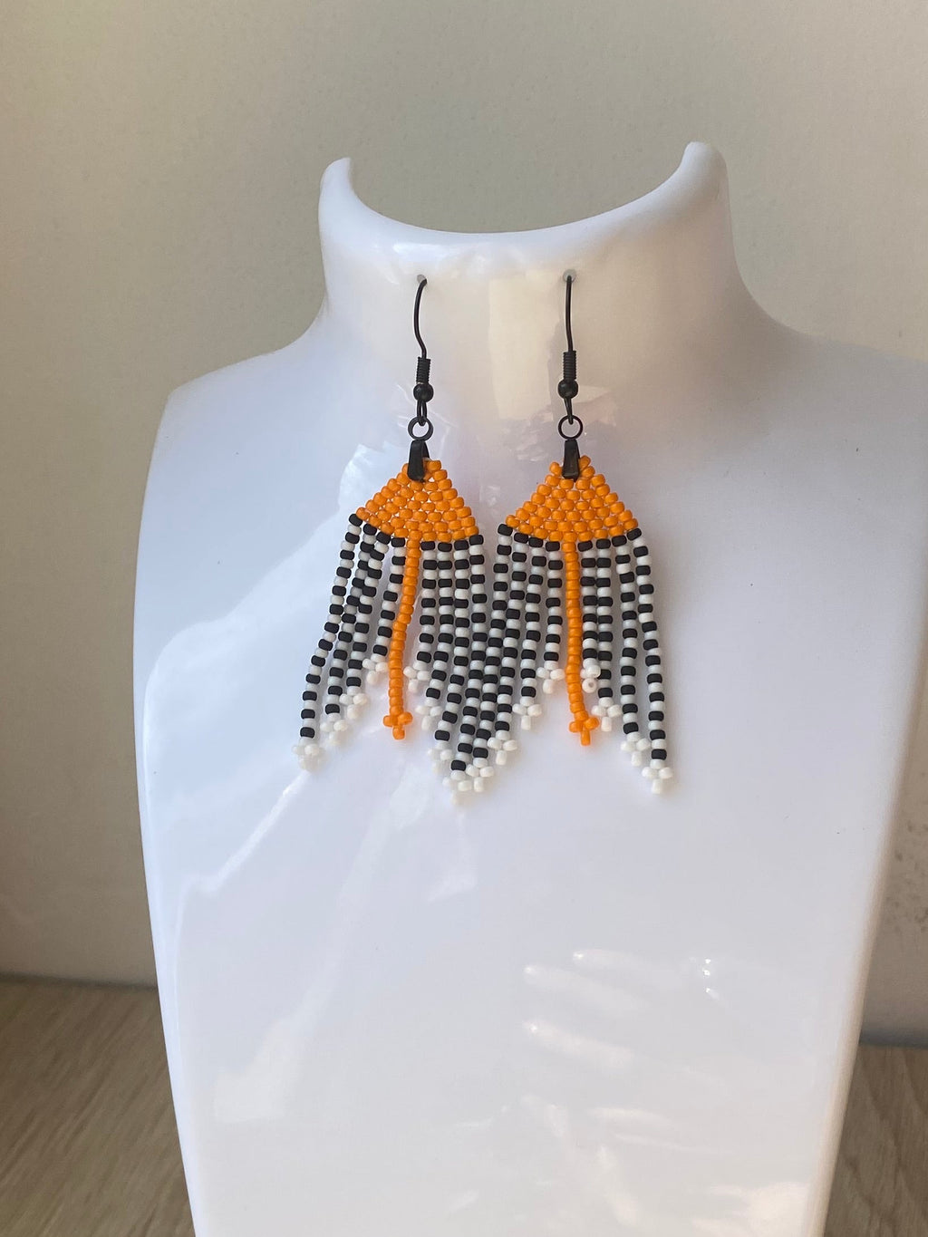 Paire de boucles d’oreilles à franges orange, noir et blanc sur présentoir