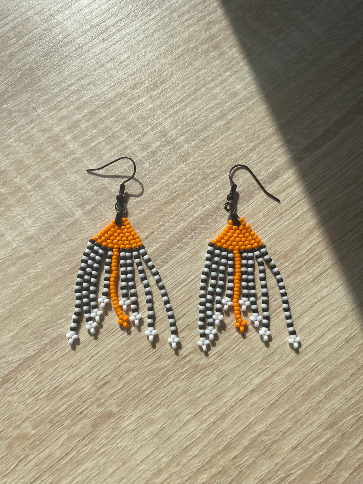 Paire de boucles d’oreilles à franges orange, noir et blanc sur présentoir, vue d’ensemble