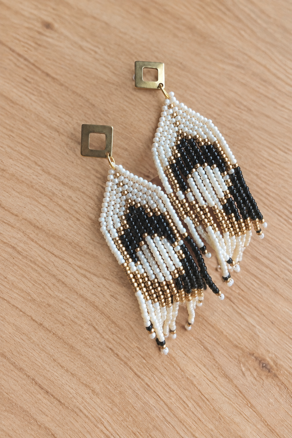 Boucles d’oreilles pendantes crème, noir et doré vieilli sans main sur fond bois clair