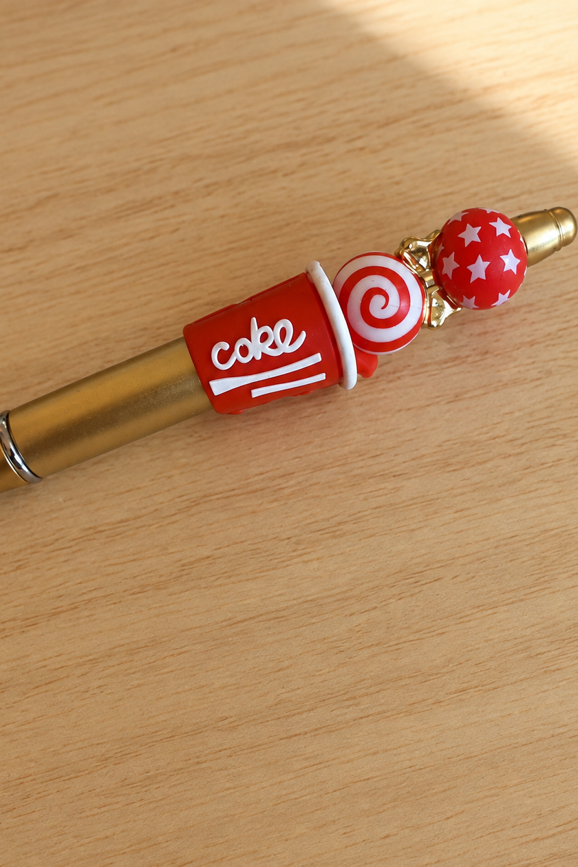 Détail du stylo soda cola rouge et doré sur bois clair