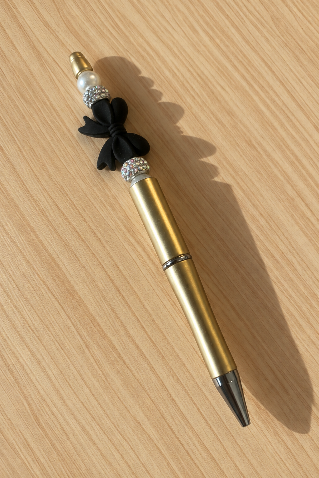 Vue entière du stylo doré à nœud noir sur bois clair