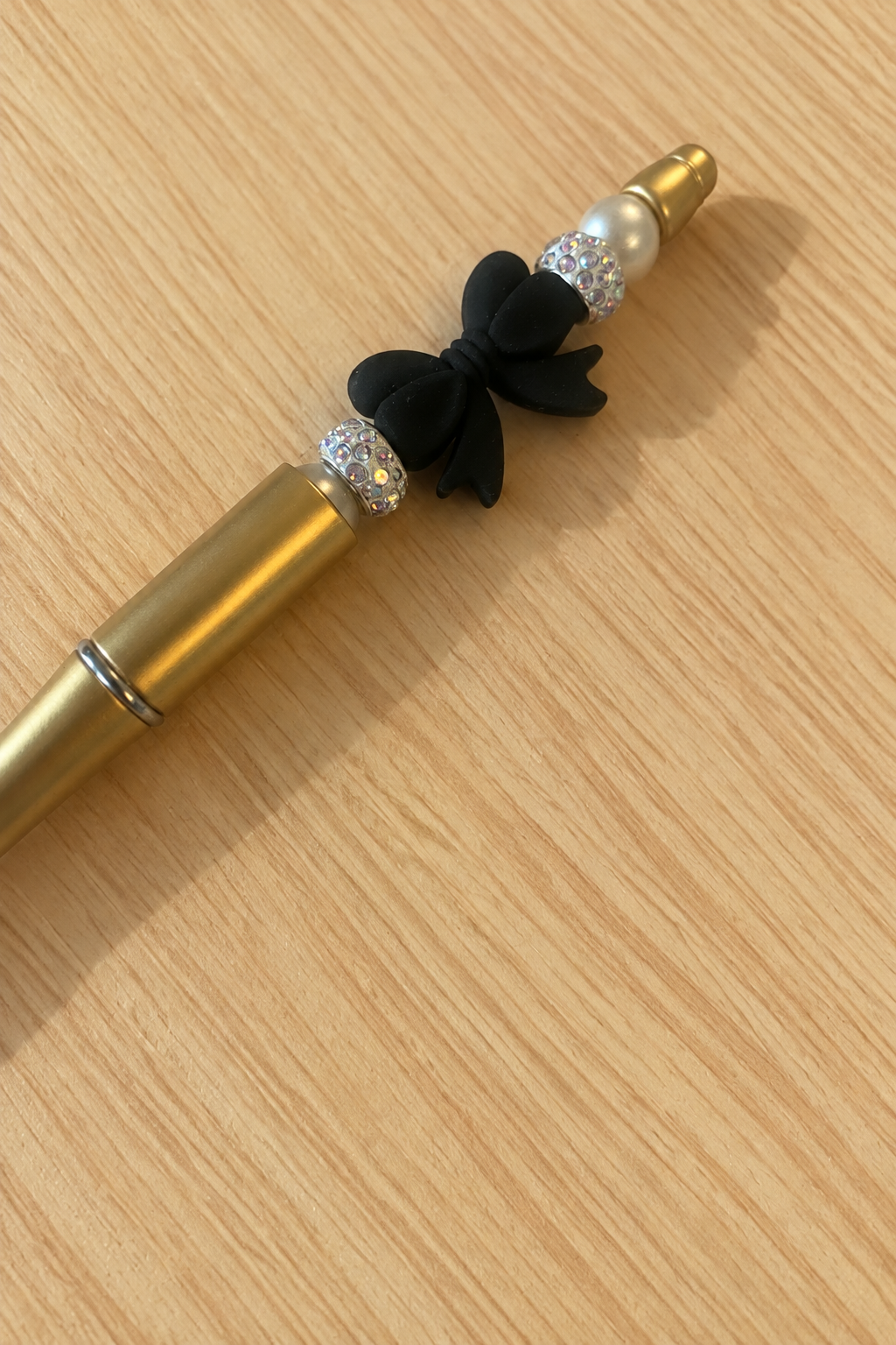 Stylo doré à nœud noir et strass en diagonale sur bois clair