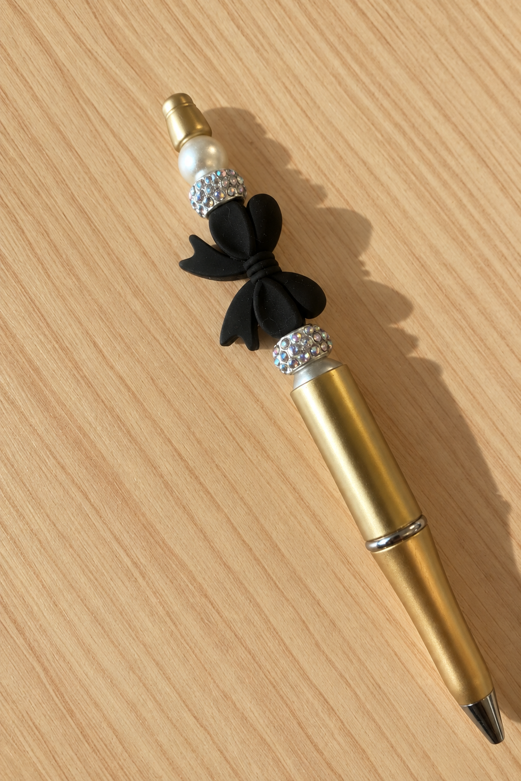 Vue rapprochée du stylo doré à gros nœud noir et strass sur bois clair