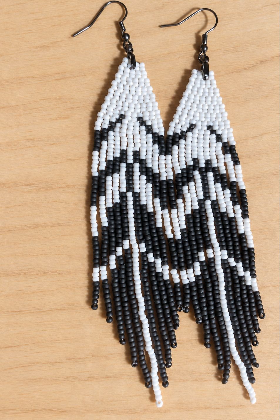 Boucles d’oreilles longues blanches et noir mat sur fond bois clair, sans mètre ruban