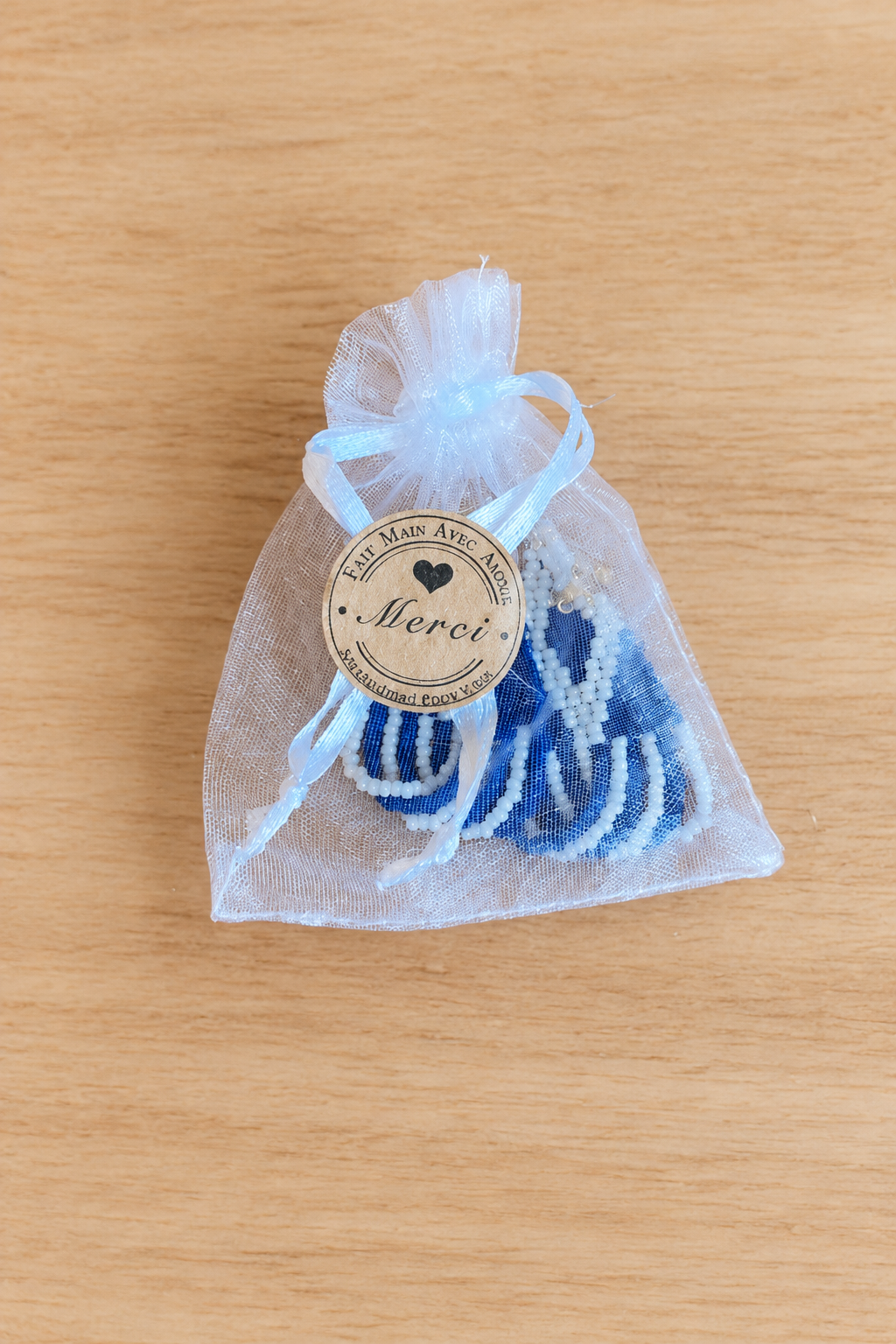 Boucles d’oreilles Miyuki blanches et bleu marine dans un sachet sur fond bois clair