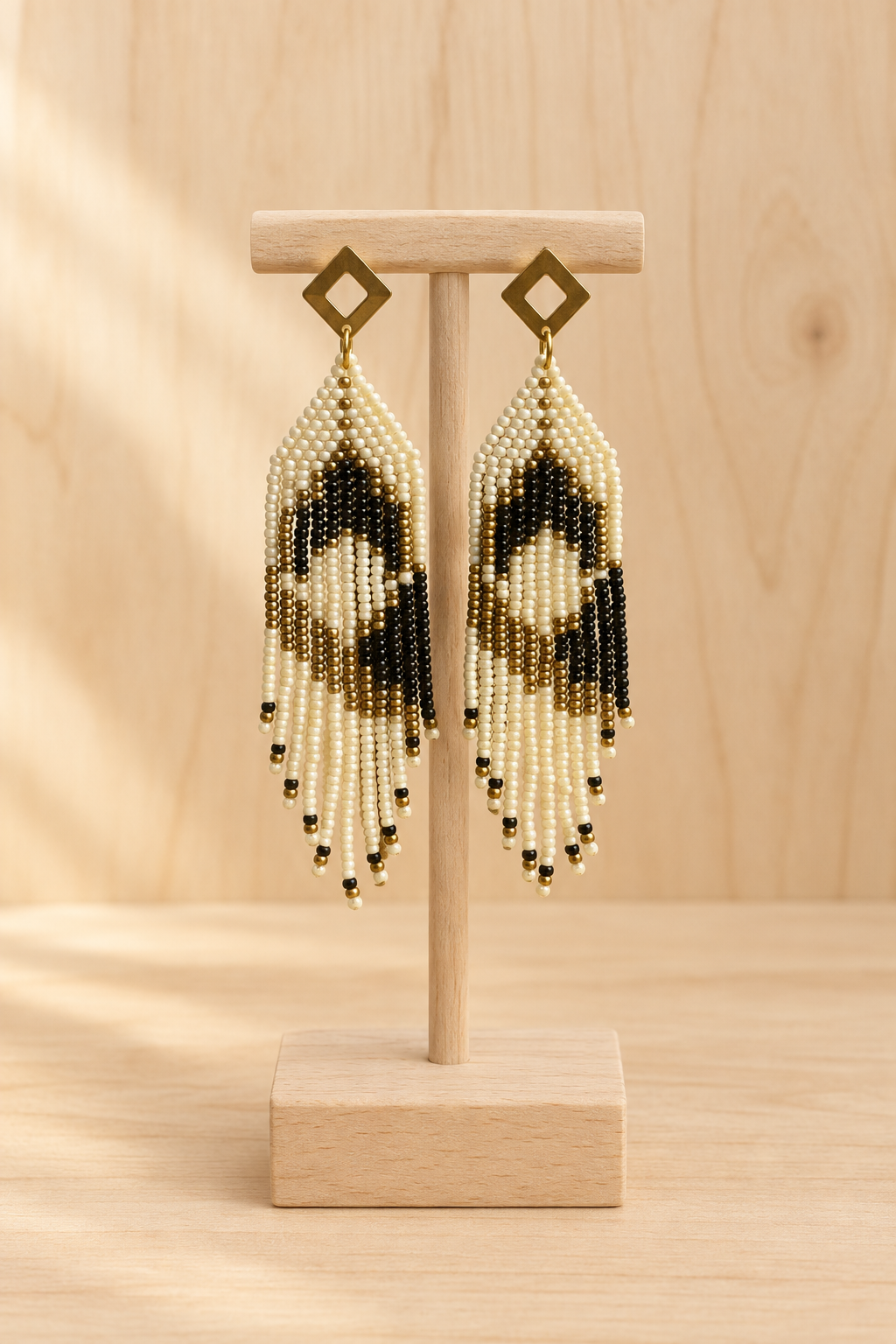 Boucles d’oreilles pendantes crème, noir et doré vieilli sur présentoir en bois clair, fond bois clair