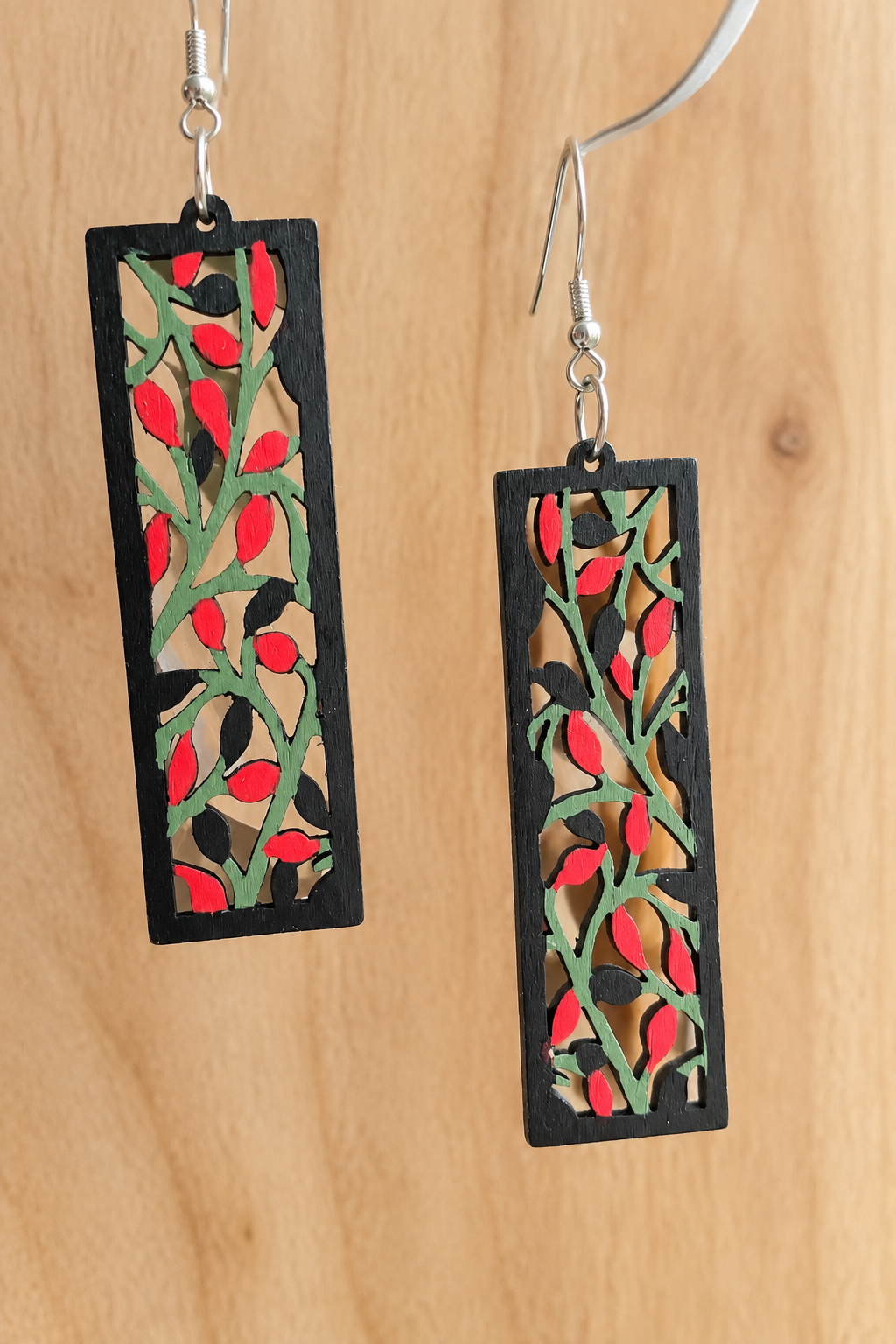 Boucles d’oreilles en bois peint branches et baies rouges sur fond bois clair