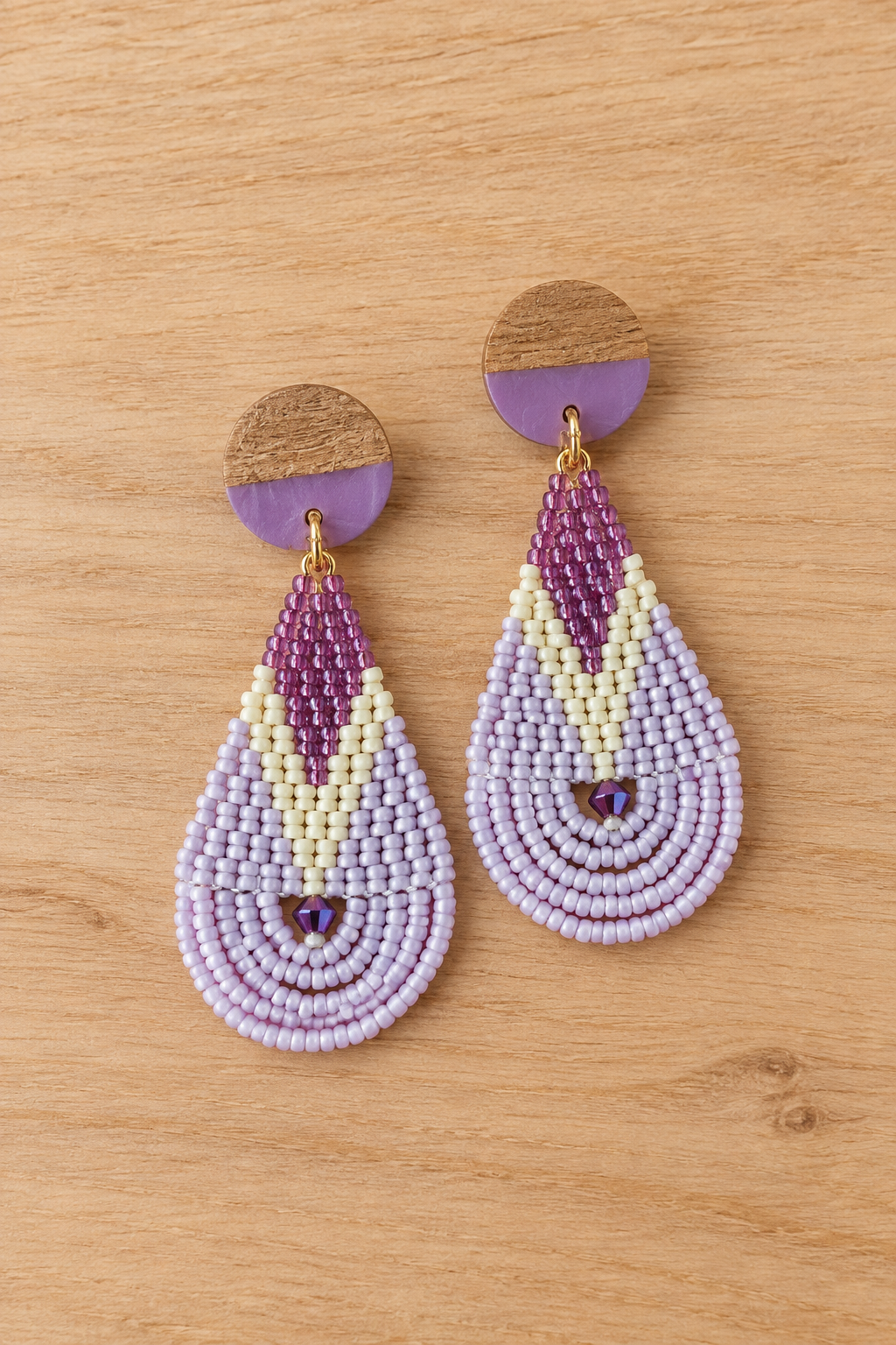 Boucles d’oreilles pendantes en perles violet, mauve et lilas sur fond bois clair