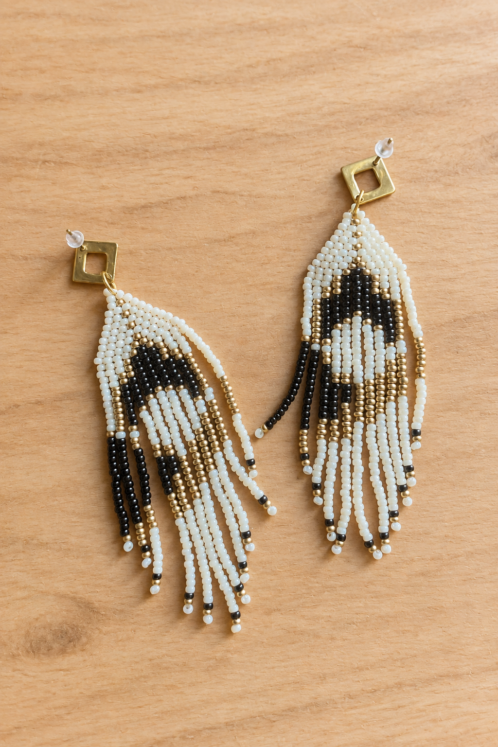 Boucles d’oreilles pendantes crème, noir et doré vieilli sur fond bois clair