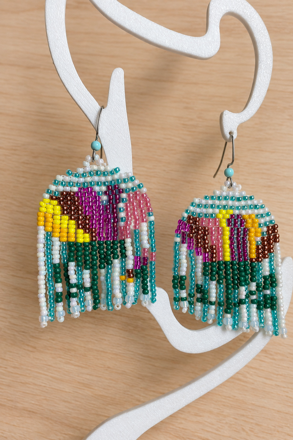 Boucles d’oreilles pendantes multicolores sur présentoir blanc, fond bois clair