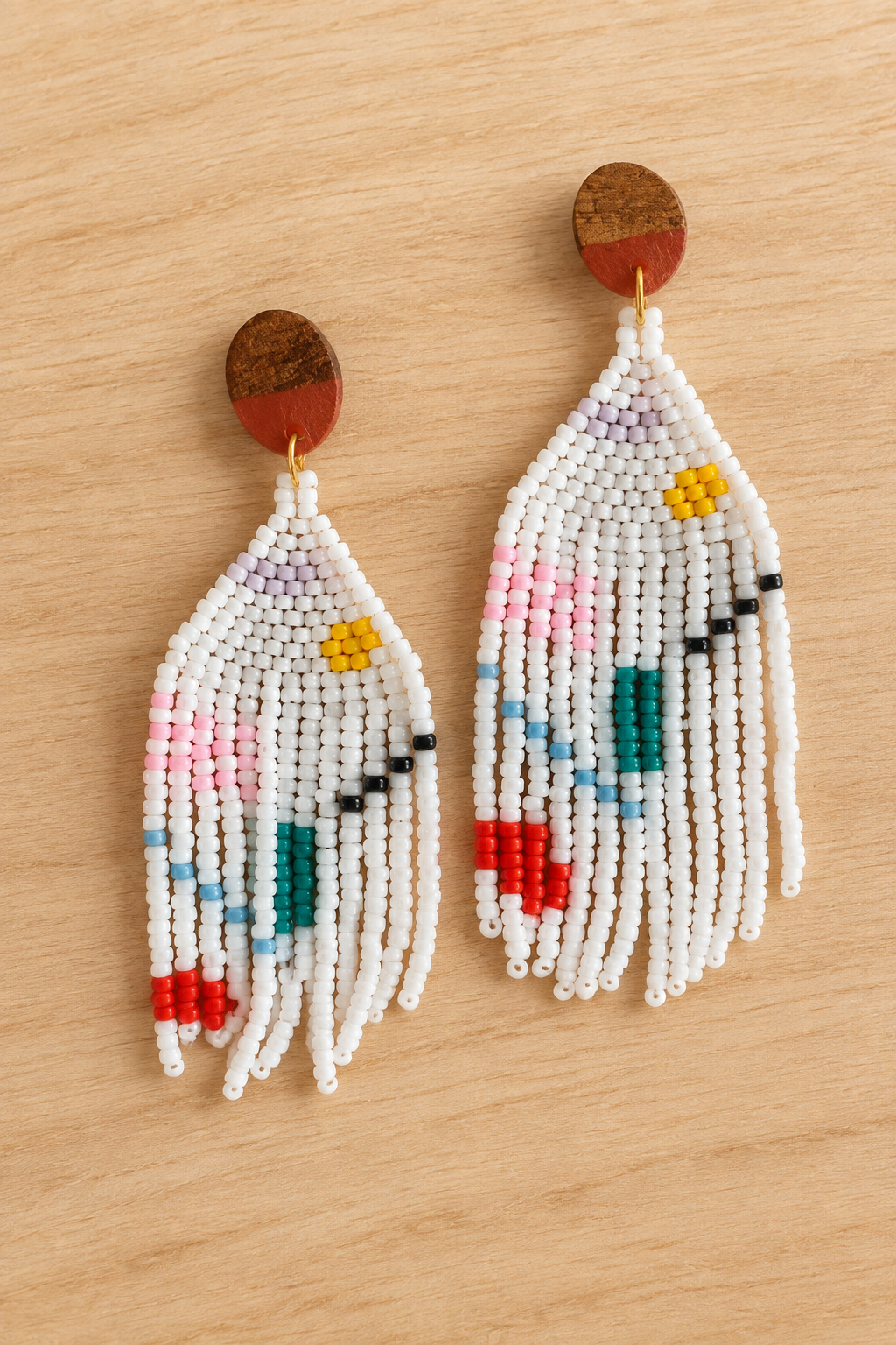 Boucles d’oreilles pendantes blanches en perles Miyuki avec motif géométrique multicolore, sur fond bois clair