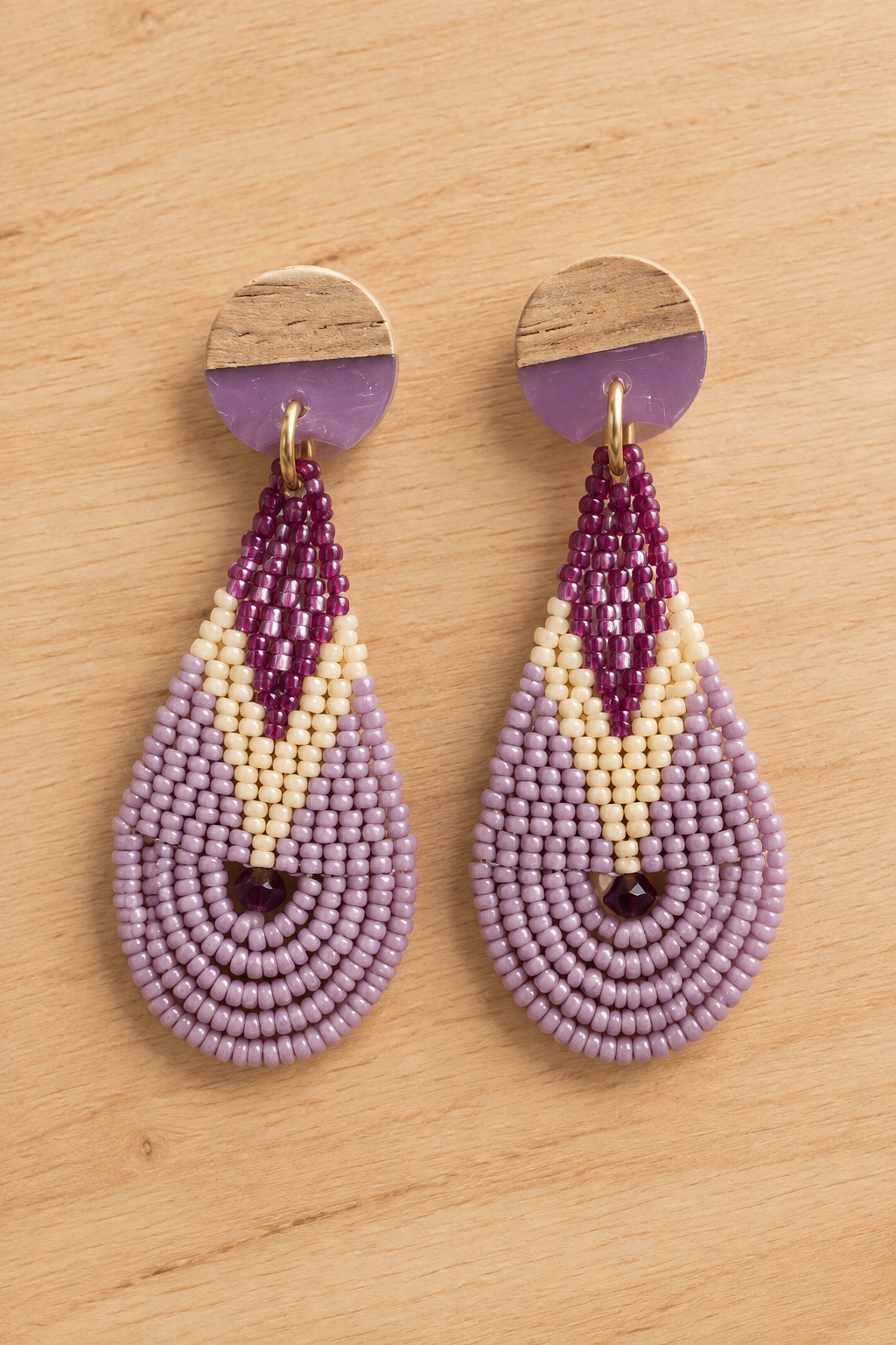 Boucles d’oreilles pendantes en perles violet, mauve et lilas sur fond bois clair