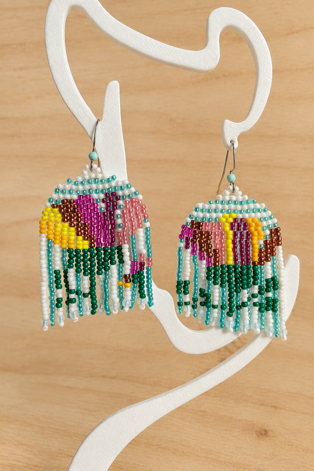 Boucles d’oreilles pendantes multicolores sur présentoir blanc, fond bois clair