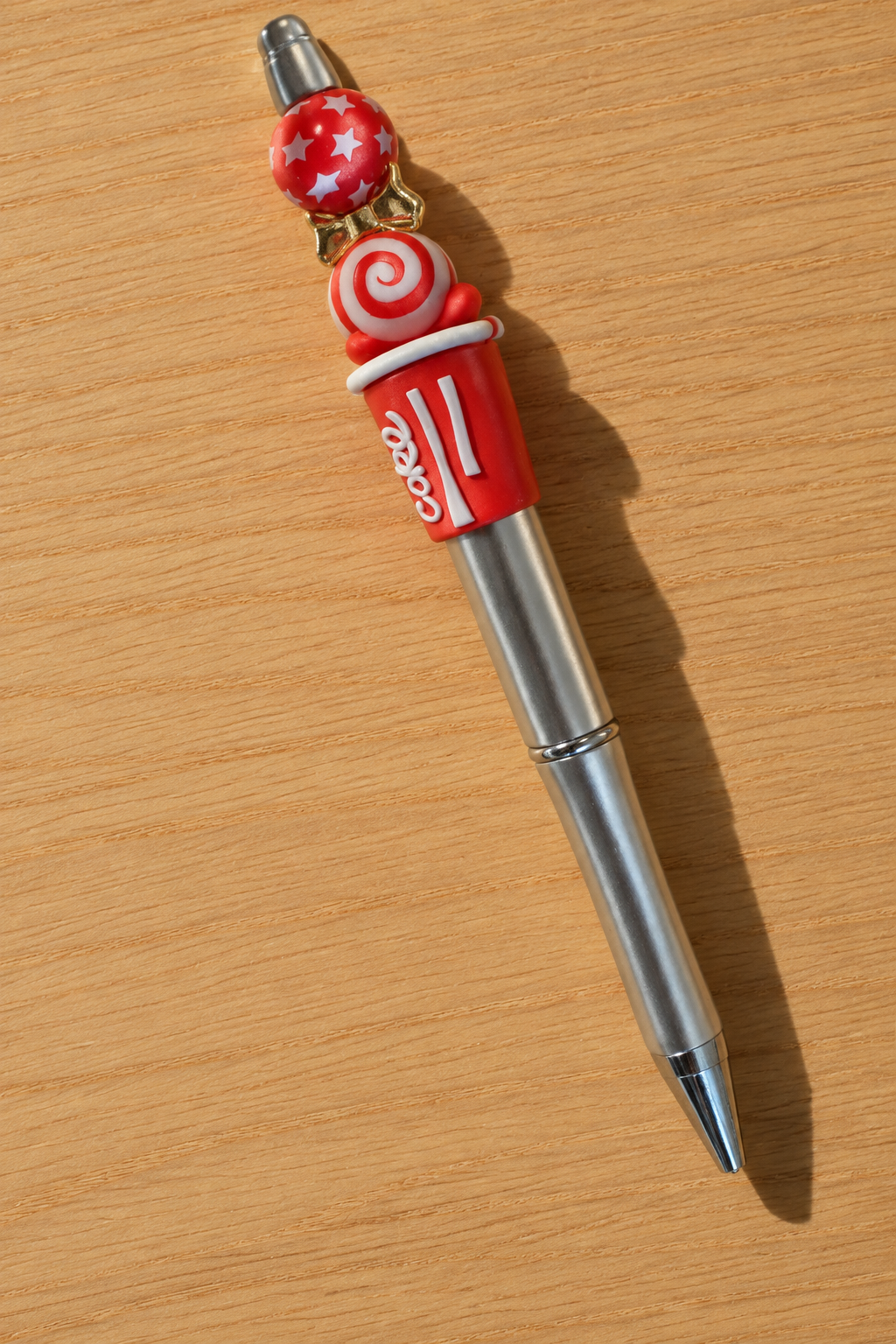 Stylo soda cola rouge et argenté à nœud doré sur bois clair