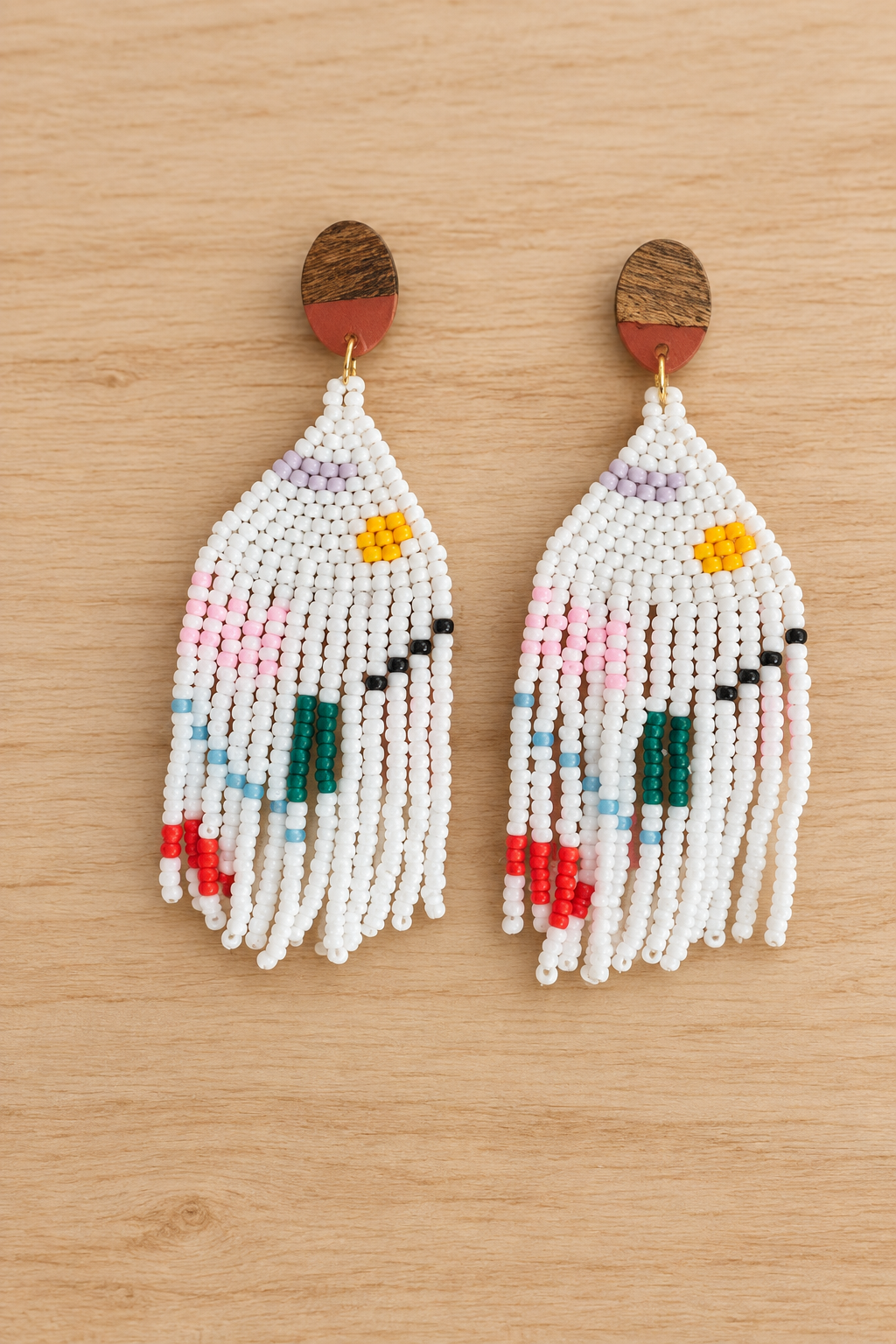 Boucles d’oreilles pendantes blanches en perles Miyuki avec motif géométrique multicolore, sur fond bois clair