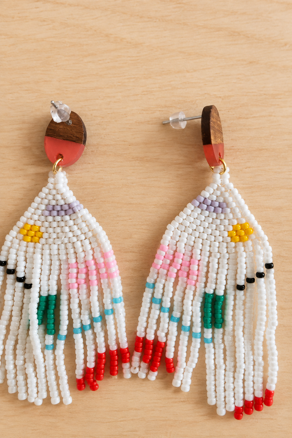 Boucles d’oreilles pendantes blanches en perles Miyuki avec motif géométrique multicolore, sur fond bois clair