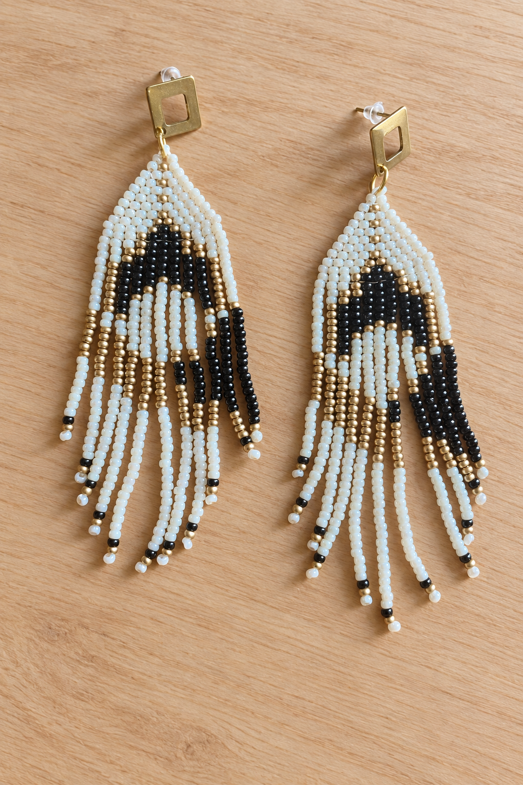 Boucles d’oreilles pendantes crème, noir et doré vieilli sur fond bois clair