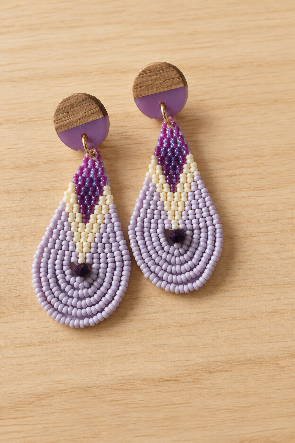 Boucles d’oreilles pendantes en perles violet, mauve et lilas sur fond bois clair
