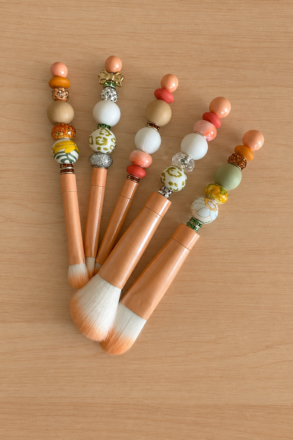 Pinceaux à maquillage pêche disposés en éventail sur bois clair