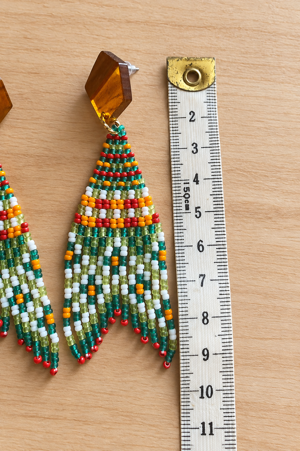 Boucle d’oreille Miyuki melon pastèque et petite croix orange avec mesure sur fond bois clair